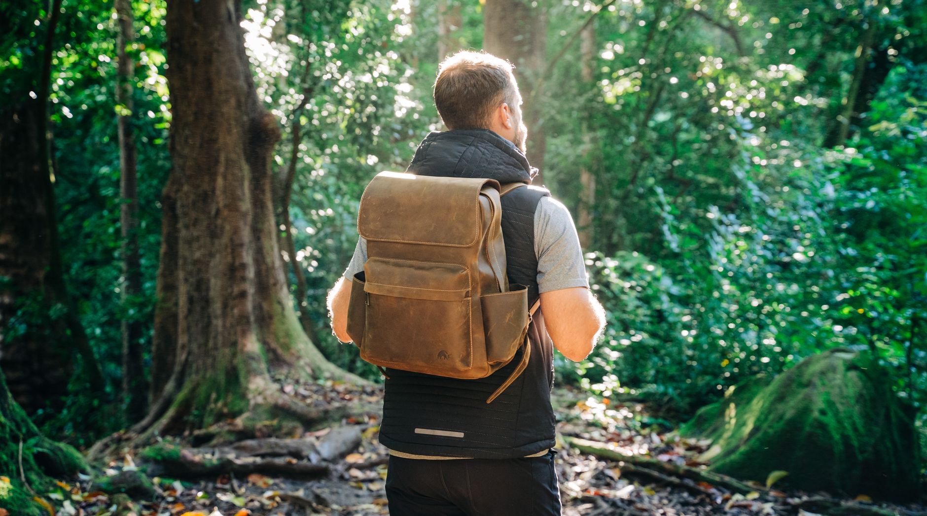 back view of a person carrying a leather backpack at a forest